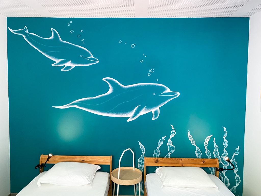 Blaue Wand mit Wandmalerei, auf der Delfine zu sehen sind.