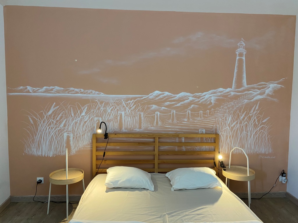 Pfirsichfarbene Wand mit einer Wandmalerei, auf der ein Leuchtturm und Strand zu sehen ist.