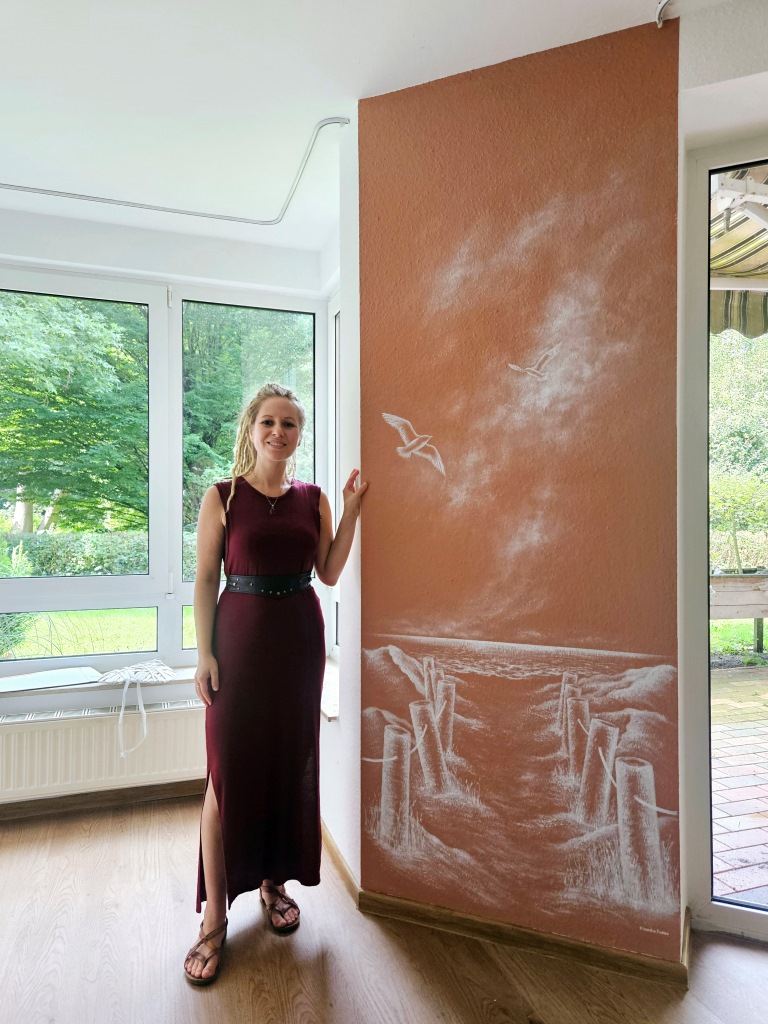 Zimmer mit terracottafarbener Wand und einem Gemälde, auf dem ein Strandzugang zu sehen ist.