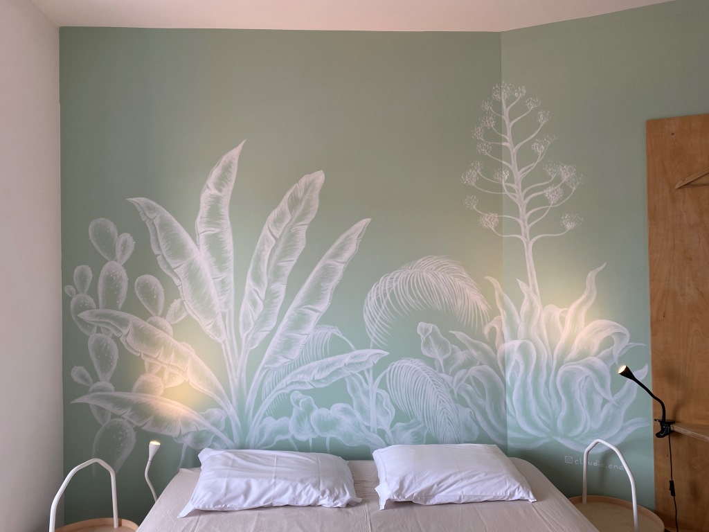 Hostelzimmer mit grüner Wand und Wandmalerei mit verschiedenen Pflanzen.