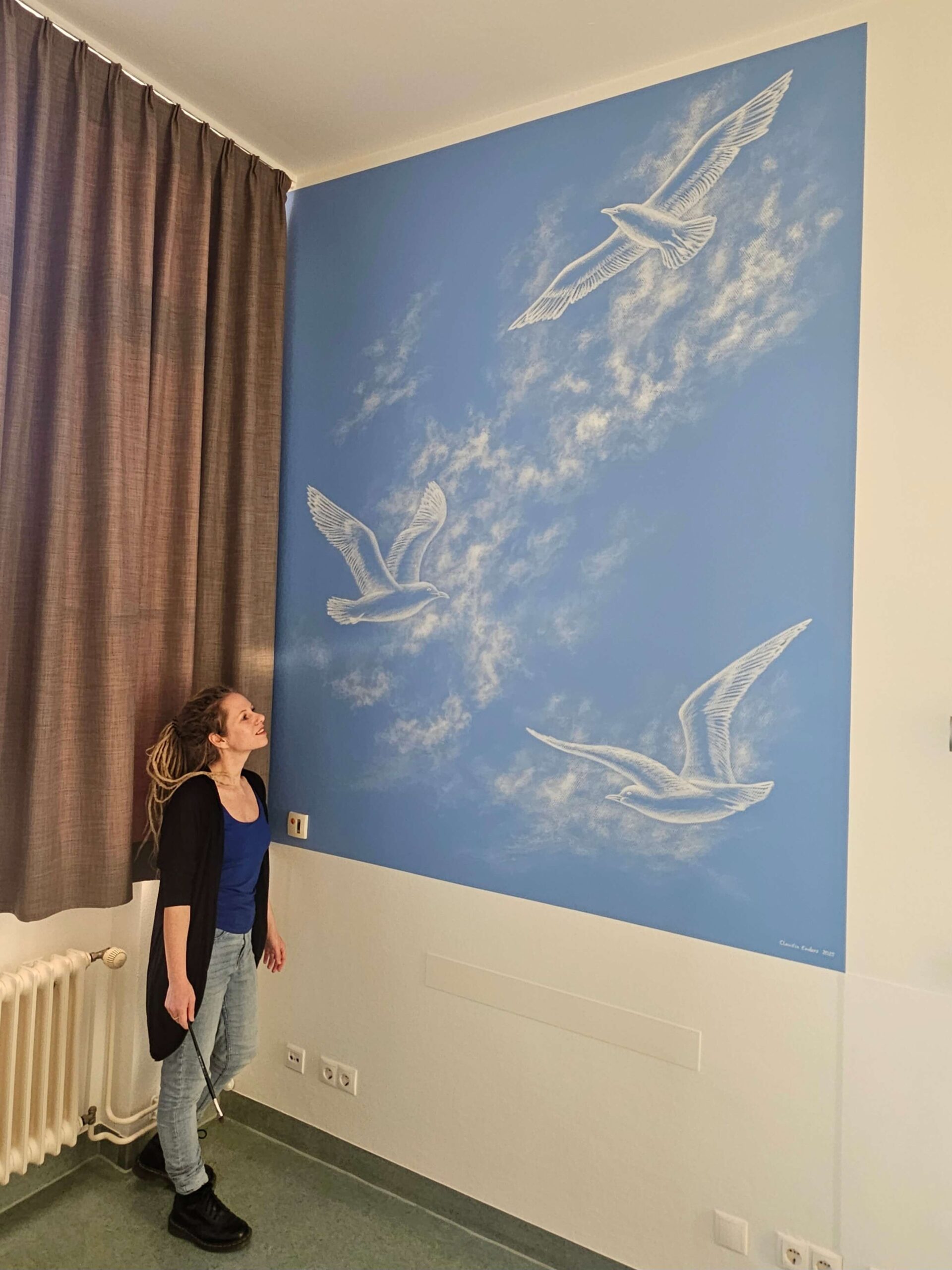 3 gemalte Möwen mit Blick in die Wolken auf einer blauen Wand.