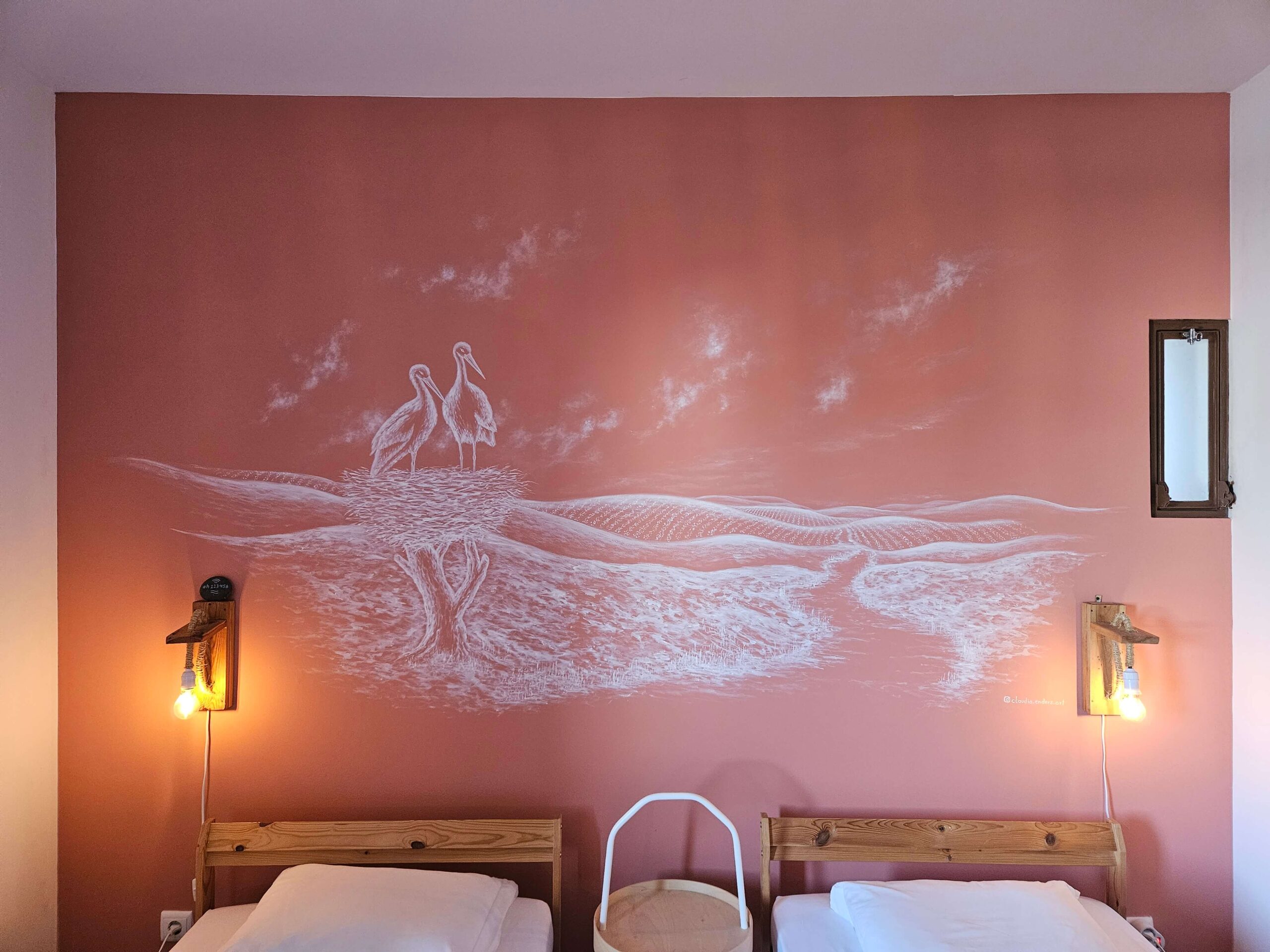Terracottafarbene Wand mit einer Wandmalerei, auf der Störche in ihrem Nest abgebildet sind.
