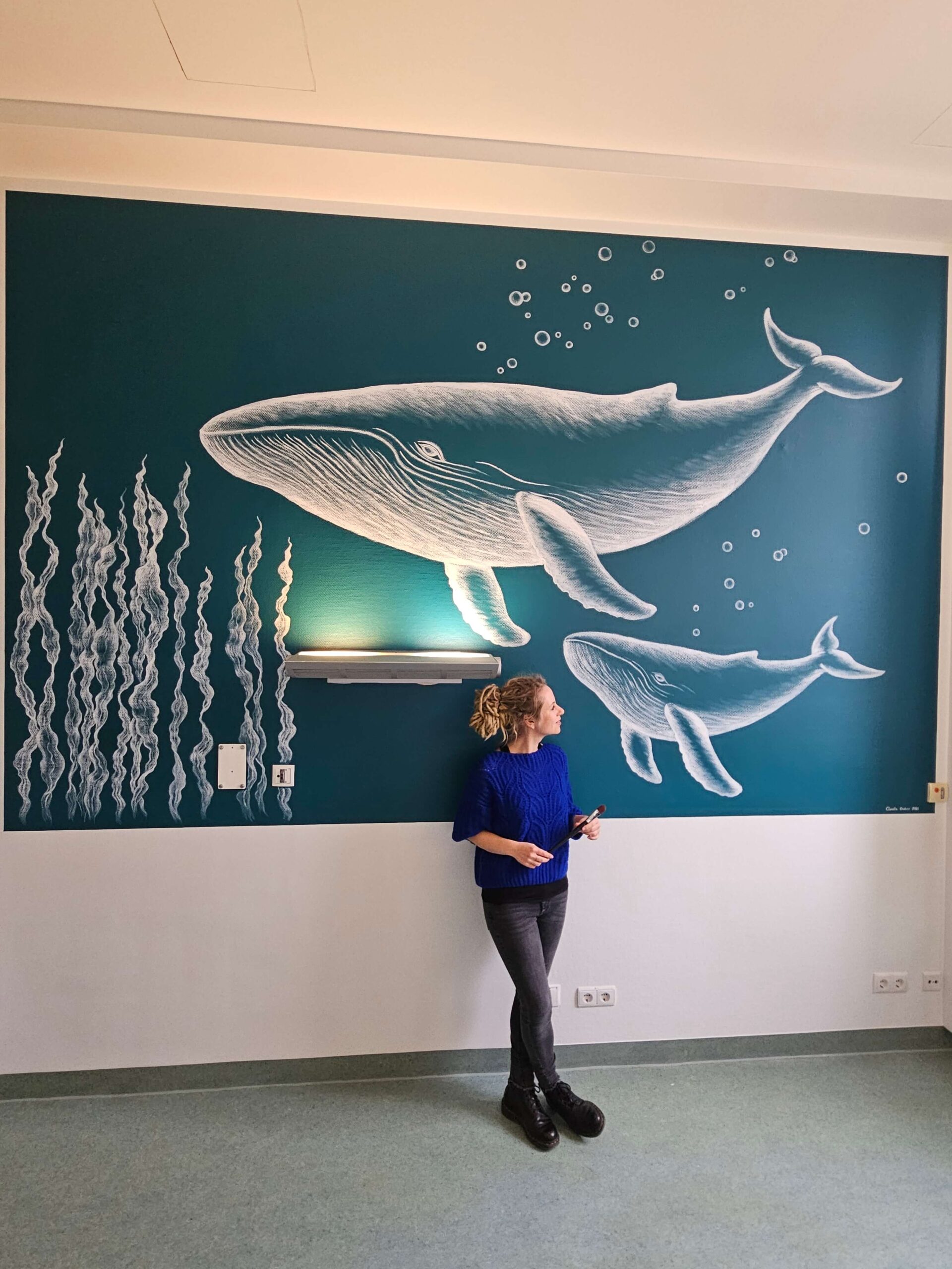 Petrolfarbene Wand mit einer Wandmalerei, auf der ein Wal und sein Kalb zu sehen sind.