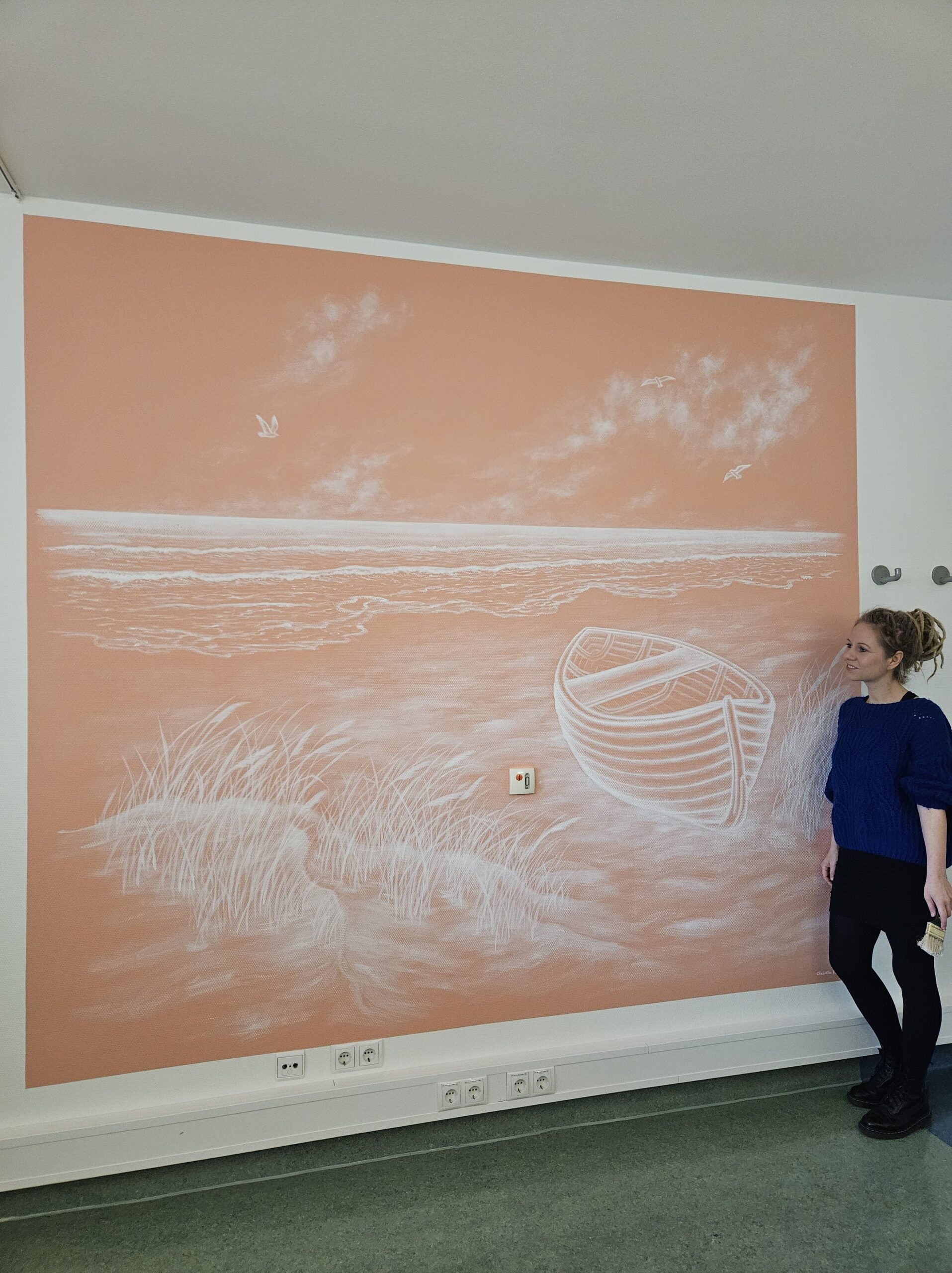 Lachsfarbene Wand mit einem Wandgemälde in Weiß, auf dem ein Boot an einem Strand zu sehen ist.