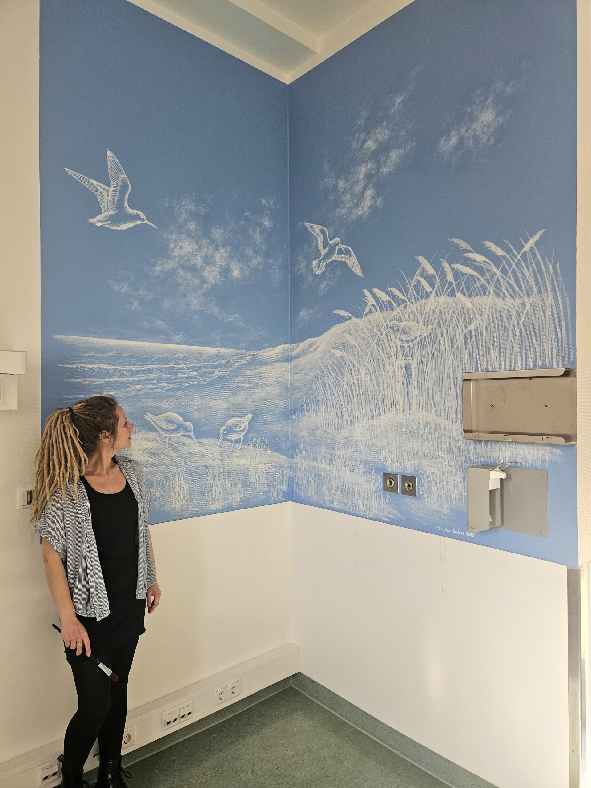 Blaue Wand mit einem weißen Wandgemälde, auf dem eine Strandszene zu sehen ist.