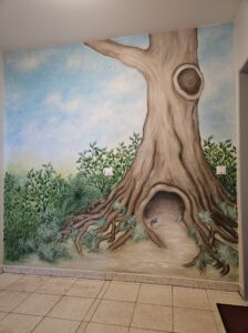 Bei dieser Wandmalerei handelt es sich um eine Treppenhausgestaltung, die einen Baum mit Baumhöhle zeigt, in der Mäuse leben.