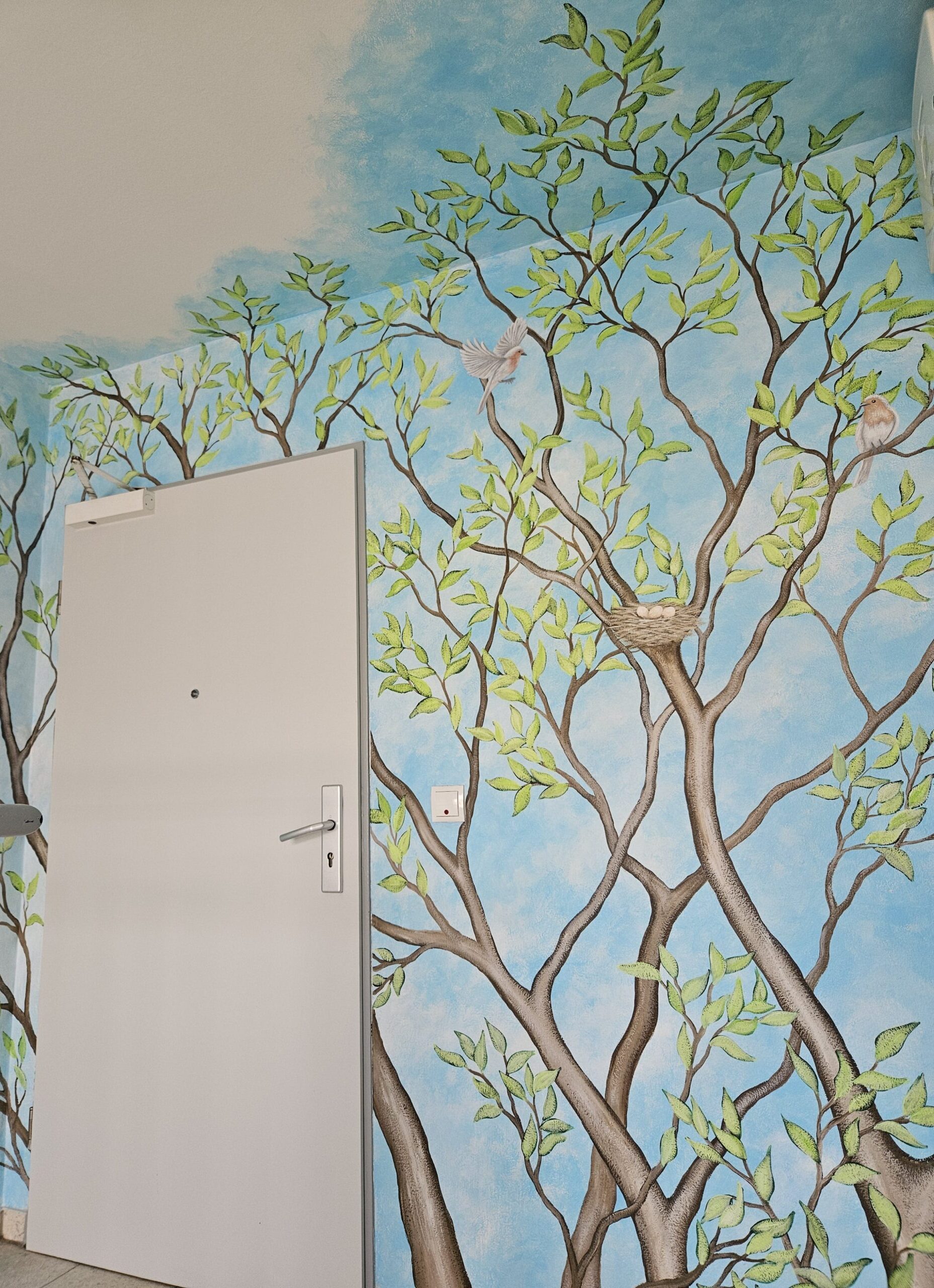 Zu sehen ist eine Treppenhausgestaltung mit einer Wandmalerei, die eine Baumkrone zeigt.