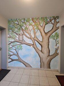 Die zweite Etage der Treppenhausgestaltung im Kinderhaus zeigt einen Baum, mit weit verzweigten Ästen, auf dem eine Eule sitzt und ein kleiner Wurm kriecht.