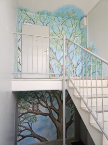 Zu sehen ist eine Wandmalerei über zwei Etagen in einem Treppenhaus.