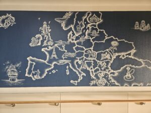 Weiße Malerei auf blauem Grund. Zu sehen ist der Europa-Kontinent mit verschiedenen kleinen Symbolbildern, die die einzelnen Länder repräsentieren.