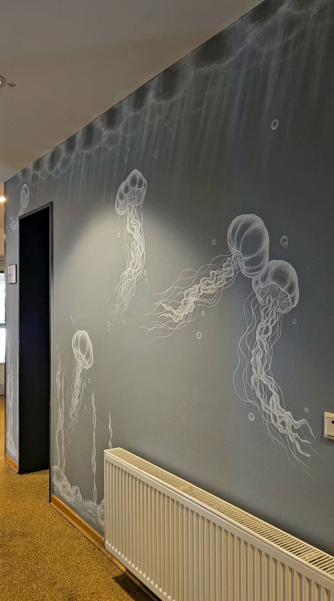 Die weiße Malerei auf grauem Untergrund zeigt einen Blick in die Unterwasserwelt zu aufsteigenden Quallen.