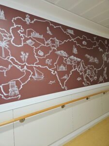Grafisches Wandgemälde des asiatischen Kontinents auf der geriatrischen Station des Agaplesion Krankenhauses. Die Karte zeigt den Kontinent mit landestypischen Symbolen und einer einfarbigen Hintergrundfläche als Teil eines Orientierungskonzepts, bei dem jeder Kontinent eine eigene Hintergrundfarbe erhält.
