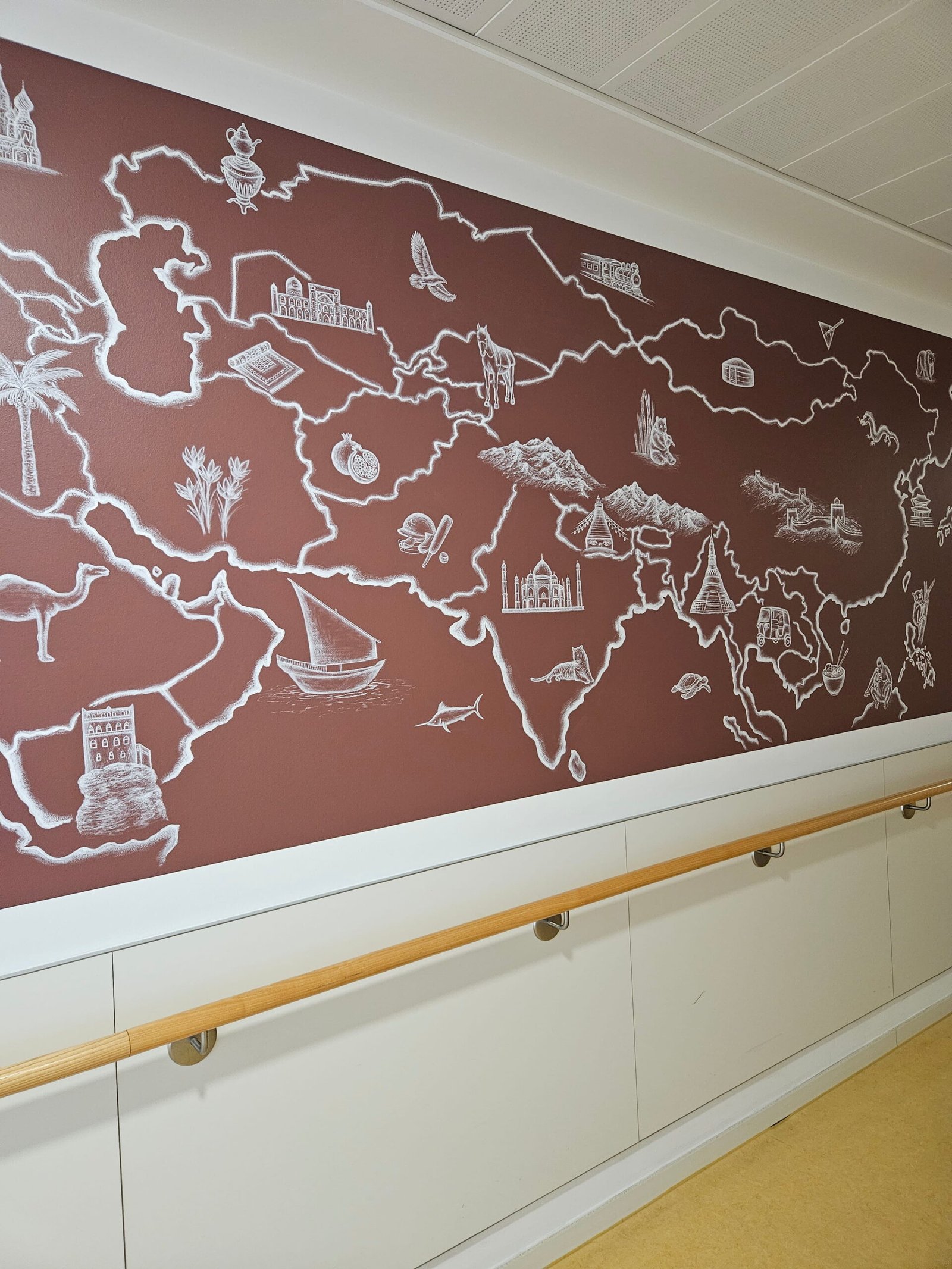 Grafisches Wandgemälde des asiatischen Kontinents auf der geriatrischen Station des Agaplesion Krankenhauses. Die Karte zeigt den Kontinent mit landestypischen Symbolen und einer einfarbigen Hintergrundfläche als Teil eines Orientierungskonzepts, bei dem jeder Kontinent eine eigene Hintergrundfarbe erhält.